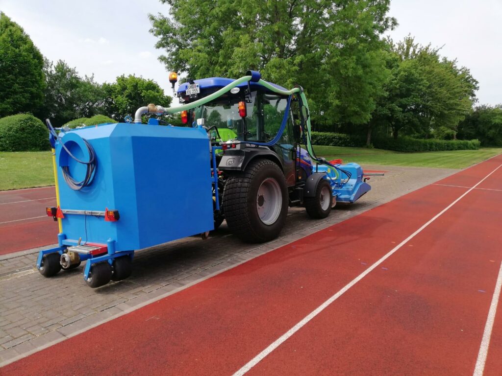 Traktor mit Tartanbahn-Reinigungsmaschine steht neben einer Tartanbahn